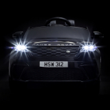 Frontansicht eines schwarzen Kinder-Elektroautos im Range-Rover-Design mit eingeschaltetem LED-Scheinwerferlicht vor schwarzem Hintergrund, Beispiel für professionelle, lichtinszenierte Produktfotografie im Bereich Spielzeug und Fahrzeuge.